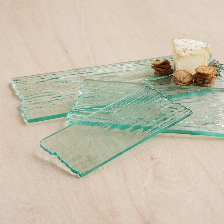 Wood grain textured clear glass rectangular cheese boards from small to large with cheese and crackers.