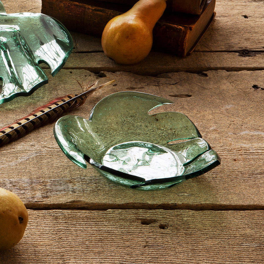 Handmade green glass bowl with a leaf pattern, displayed on a wooden surface.