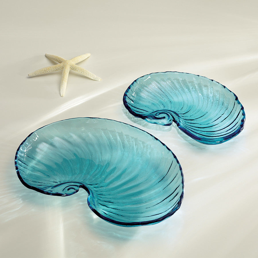 Two handmade turquoise nautilus shell-shaped serving trays on a white surface with a starfish to the side.