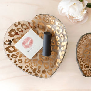 Lipstick and a small card inside a glass heart-shaped dish with 24k gold cheetah print pattern. 