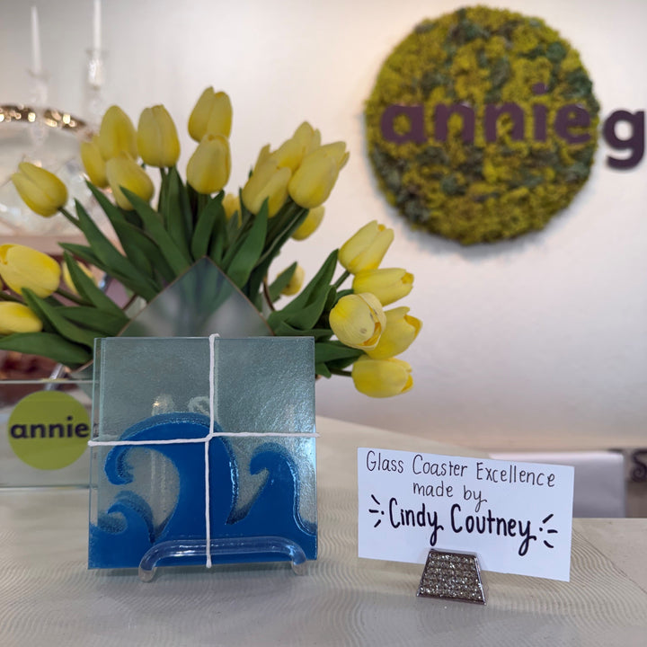 Finished set of glass coasters with ocean wave design in front of yellow tulips.