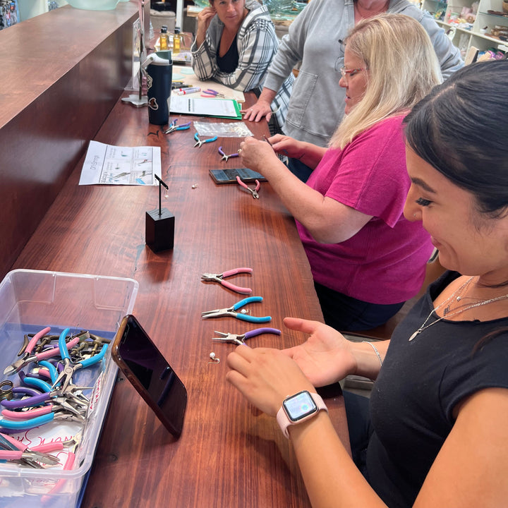 Group of people making pearl earrings at a store counter.