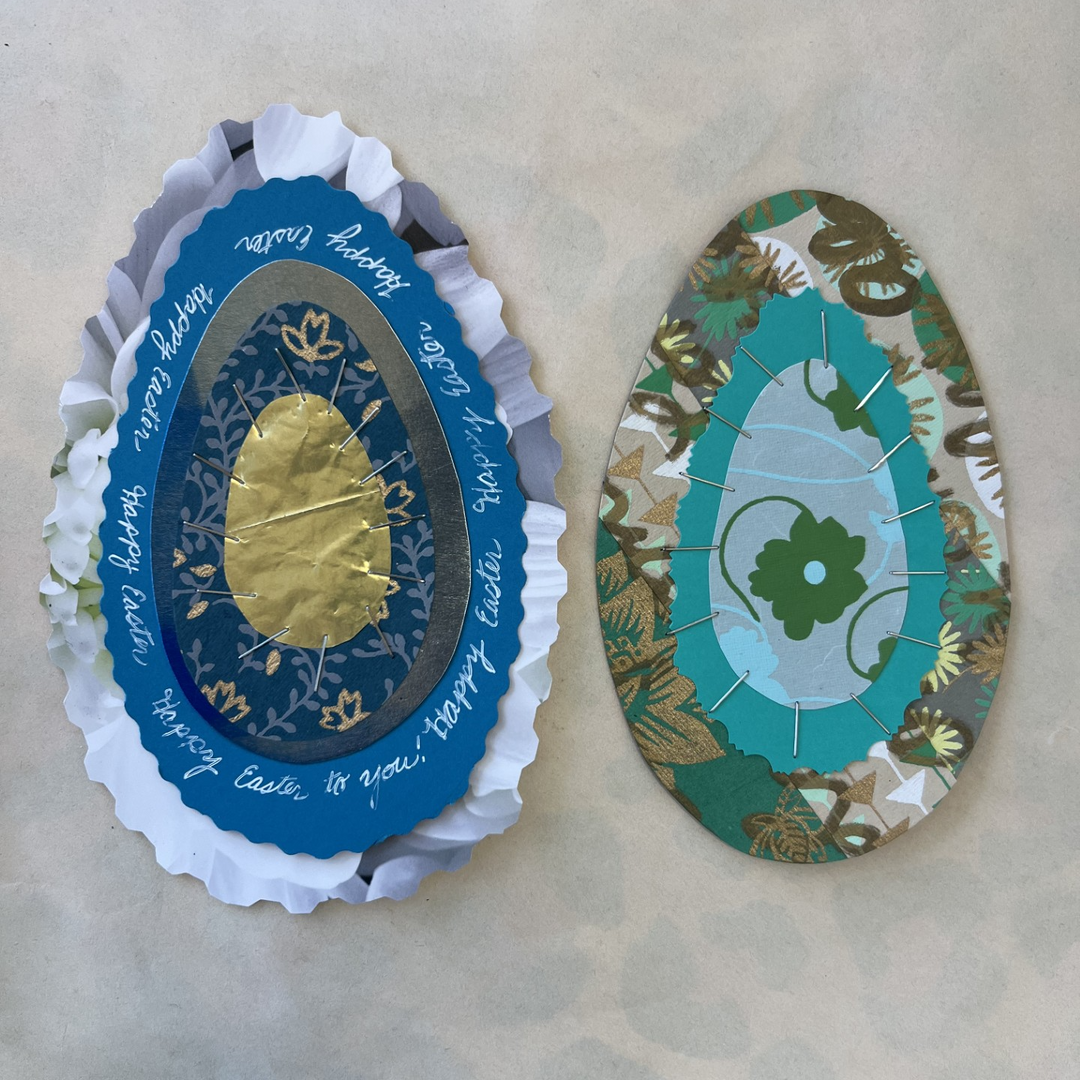 Two decorative egg-shaped paper cards with intricate designs on a beige surface