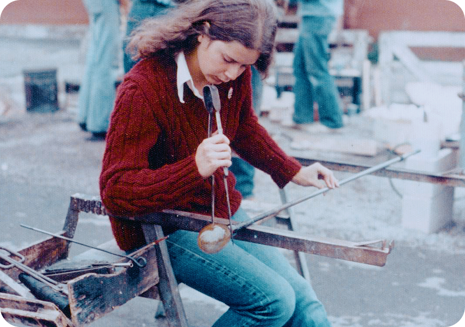 Young Annie in 1977 in a red sweater and blue jeans working with blown glass.
