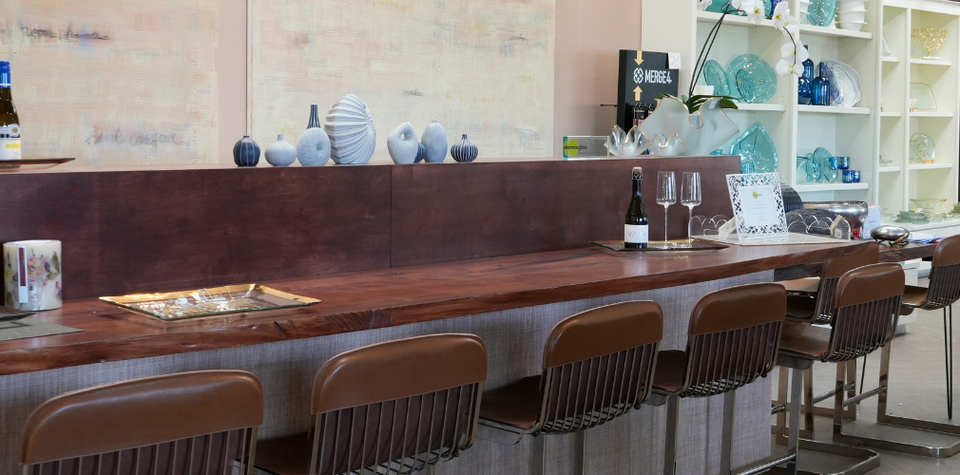 Modern bar area with wooden counter, stools, and wine glasses.