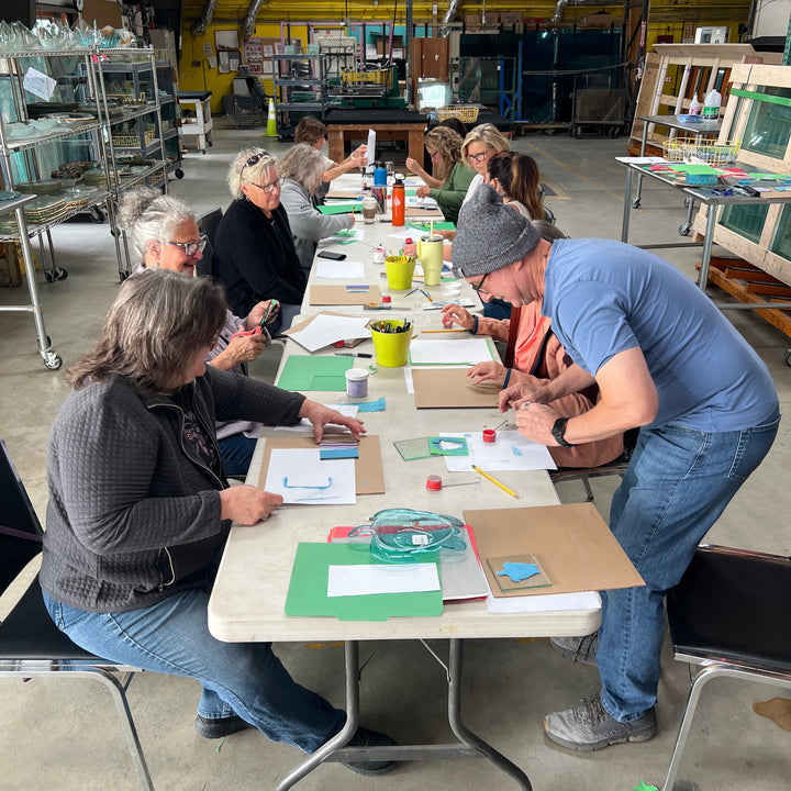 Group of people gathered around a table with glass coater making materials.